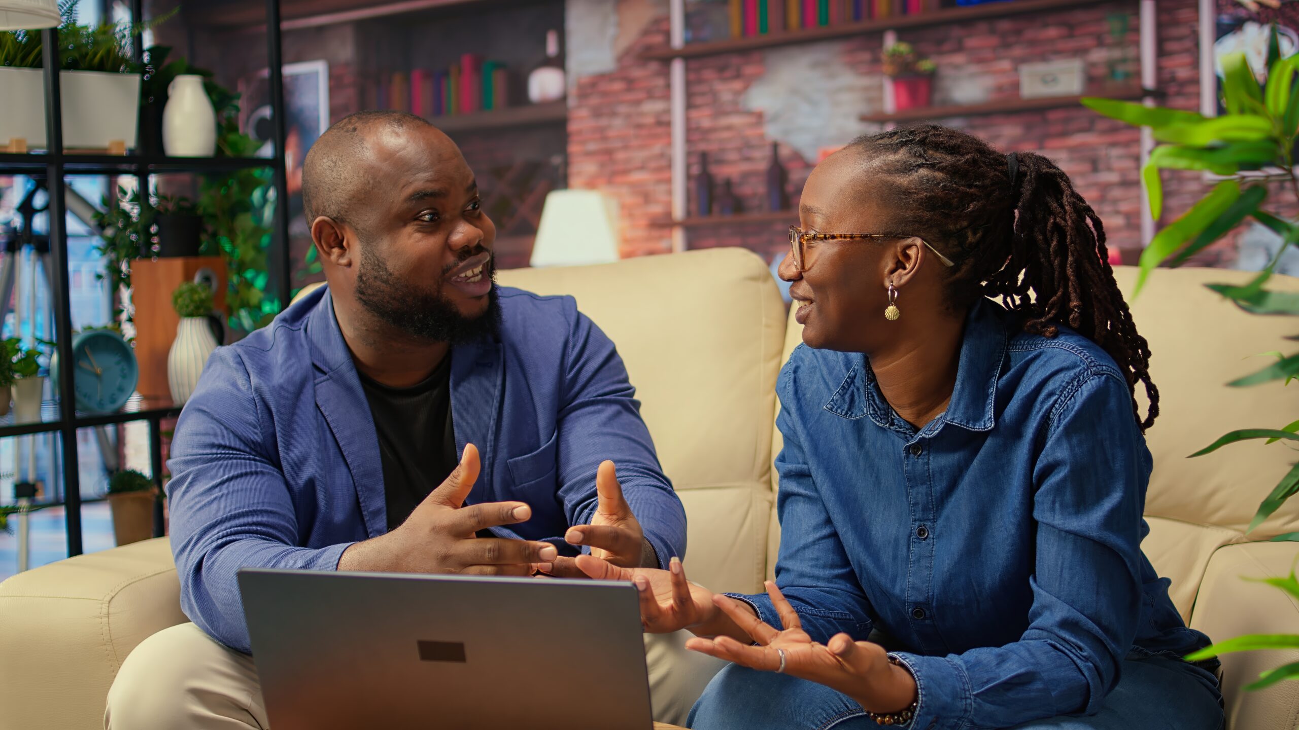 African american young freelancers on couch sharing a business idea, using modern technology and tools to analyze trends and boost success. Couple improving workflow efficiently. Camera A.
